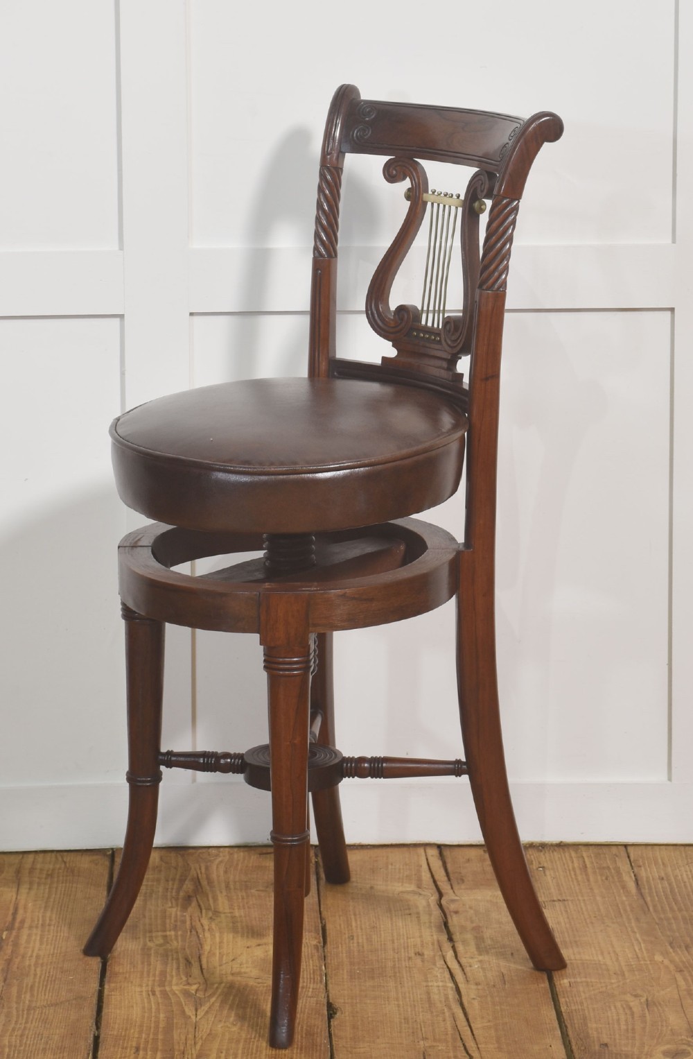 A 19th-century mahogany adjustable chair featuring a carved lyre backrest with brass details, a circular dark leather padded seat, and turned legs. View VIII
