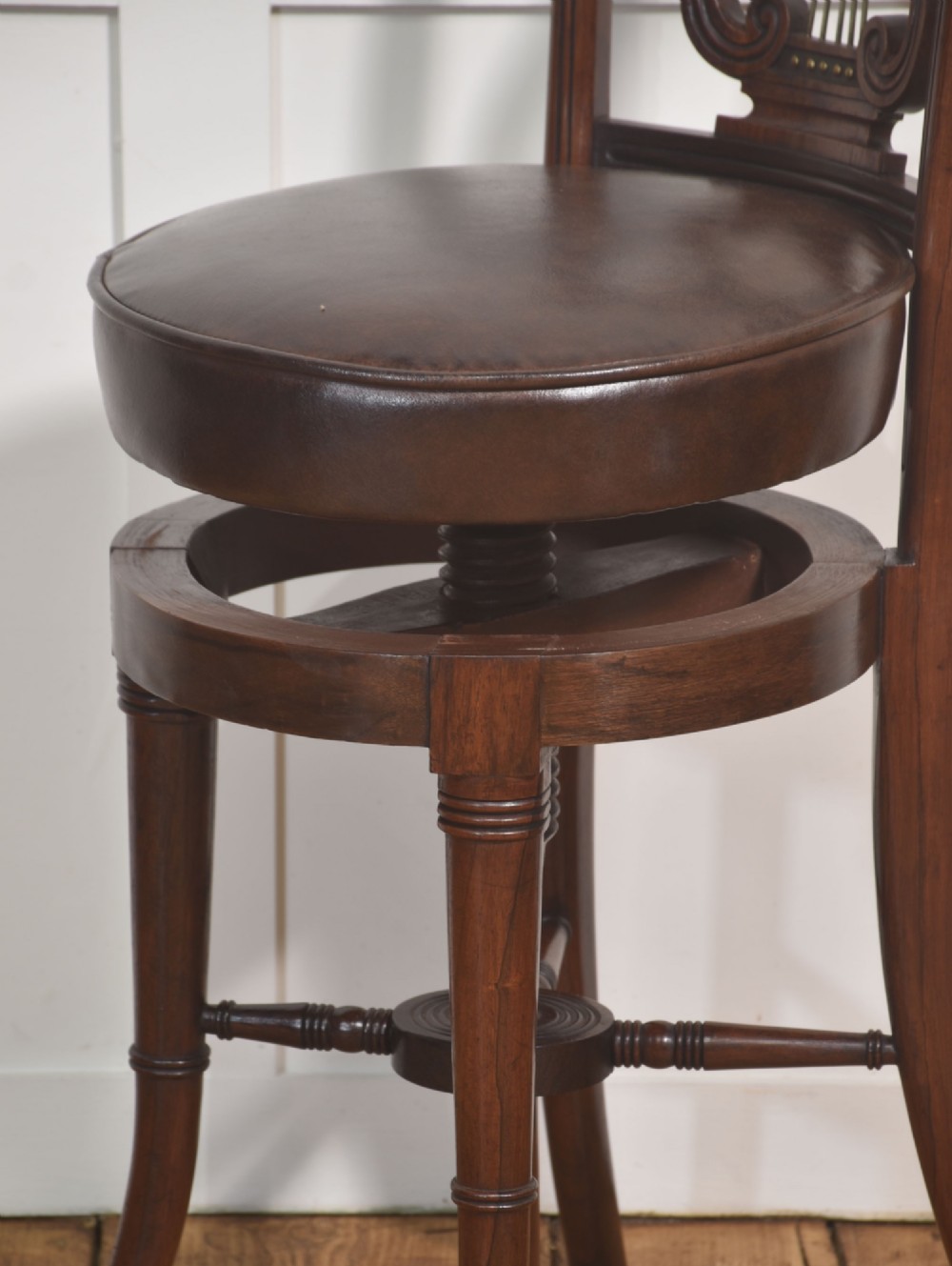 A 19th-century mahogany adjustable chair featuring a carved lyre backrest with brass details, a circular dark leather padded seat, and turned legs. View IX