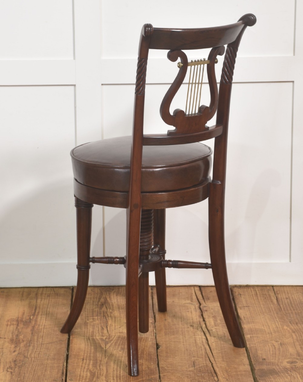 A 19th-century mahogany adjustable chair featuring a carved lyre backrest with brass details, a circular dark leather padded seat, and turned legs. View X