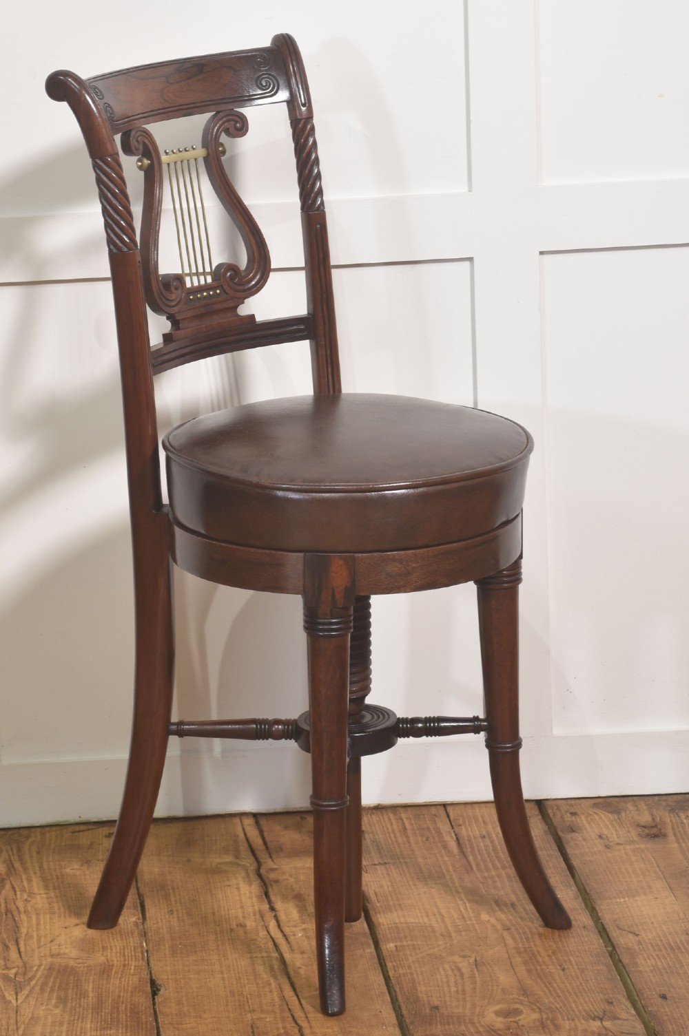 A 19th-century mahogany adjustable chair featuring a carved lyre backrest with brass details, a circular dark leather padded seat, and turned legs.