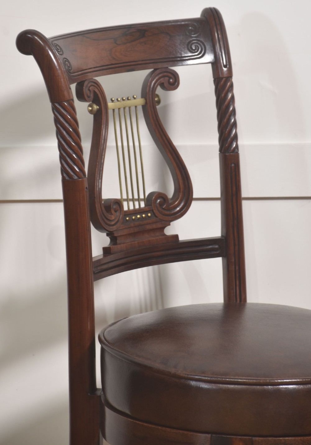 A 19th-century mahogany adjustable chair featuring a carved lyre backrest with brass details, a circular dark leather padded seat, and turned legs. View XI