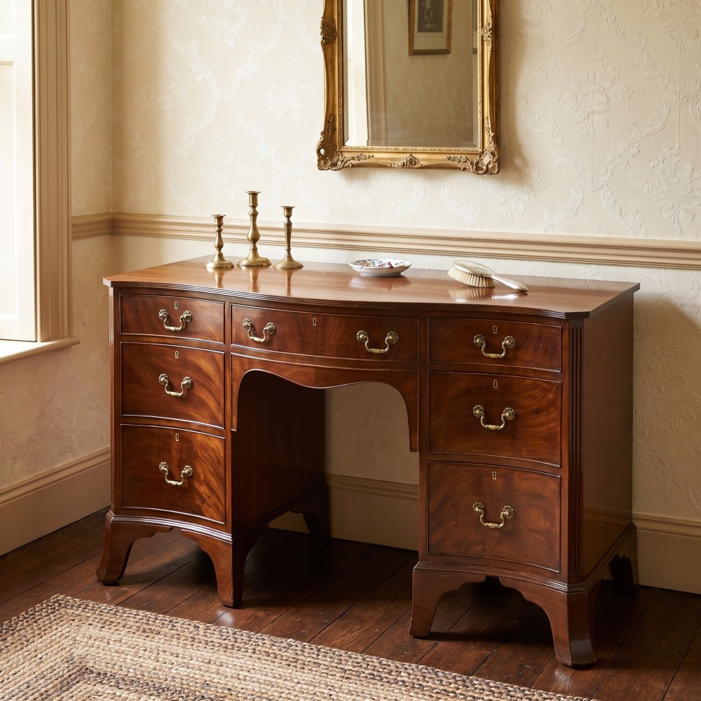 A mahogany serpentine-fronted dressing table featuring nine drawers with brass swan-neck handles and a shaped central kneehole. View II