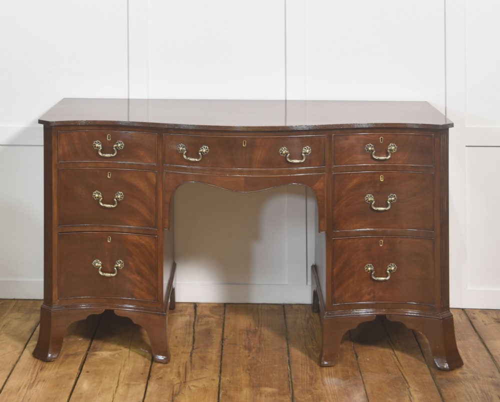 A mahogany serpentine-fronted dressing table featuring nine drawers with brass swan-neck handles and a shaped central kneehole.