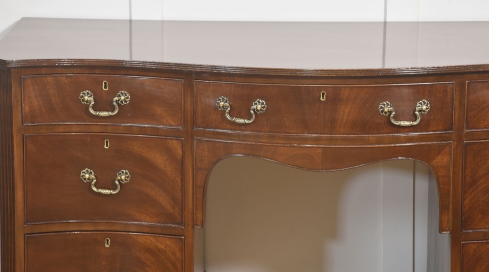 A mahogany serpentine-fronted dressing table featuring nine drawers with brass swan-neck handles and a shaped central kneehole. View III