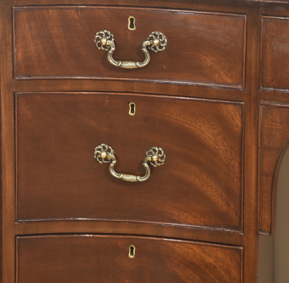 A mahogany serpentine-fronted dressing table featuring nine drawers with brass swan-neck handles and a shaped central kneehole. View V