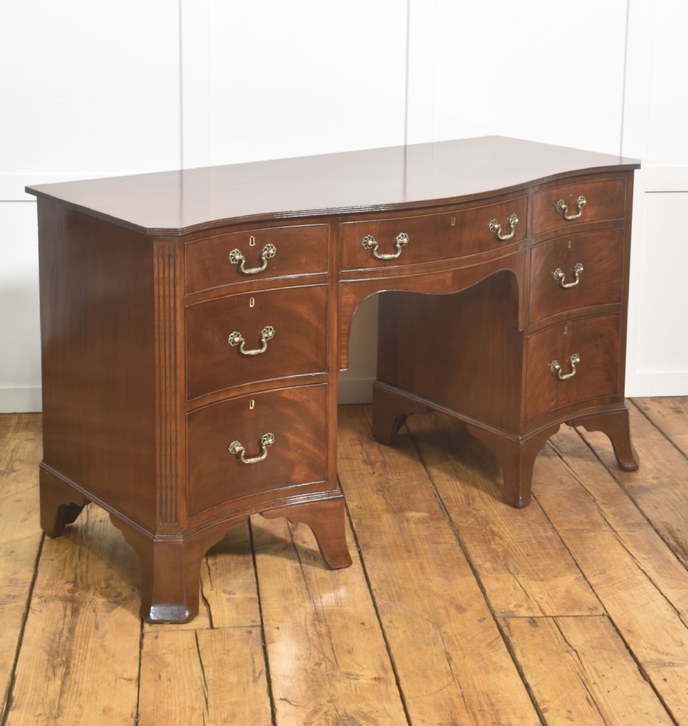 A mahogany serpentine-fronted dressing table featuring nine drawers with brass swan-neck handles and a shaped central kneehole. View VI