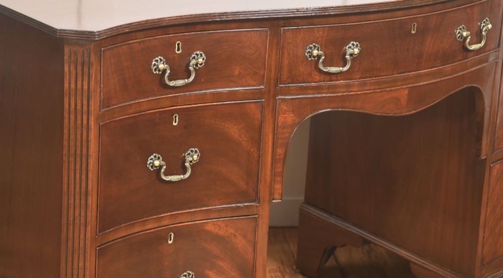 A mahogany serpentine-fronted dressing table featuring nine drawers with brass swan-neck handles and a shaped central kneehole. View VII