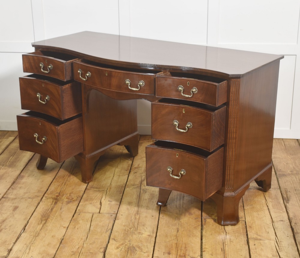 A mahogany serpentine-fronted dressing table featuring nine drawers with brass swan-neck handles and a shaped central kneehole. View IX