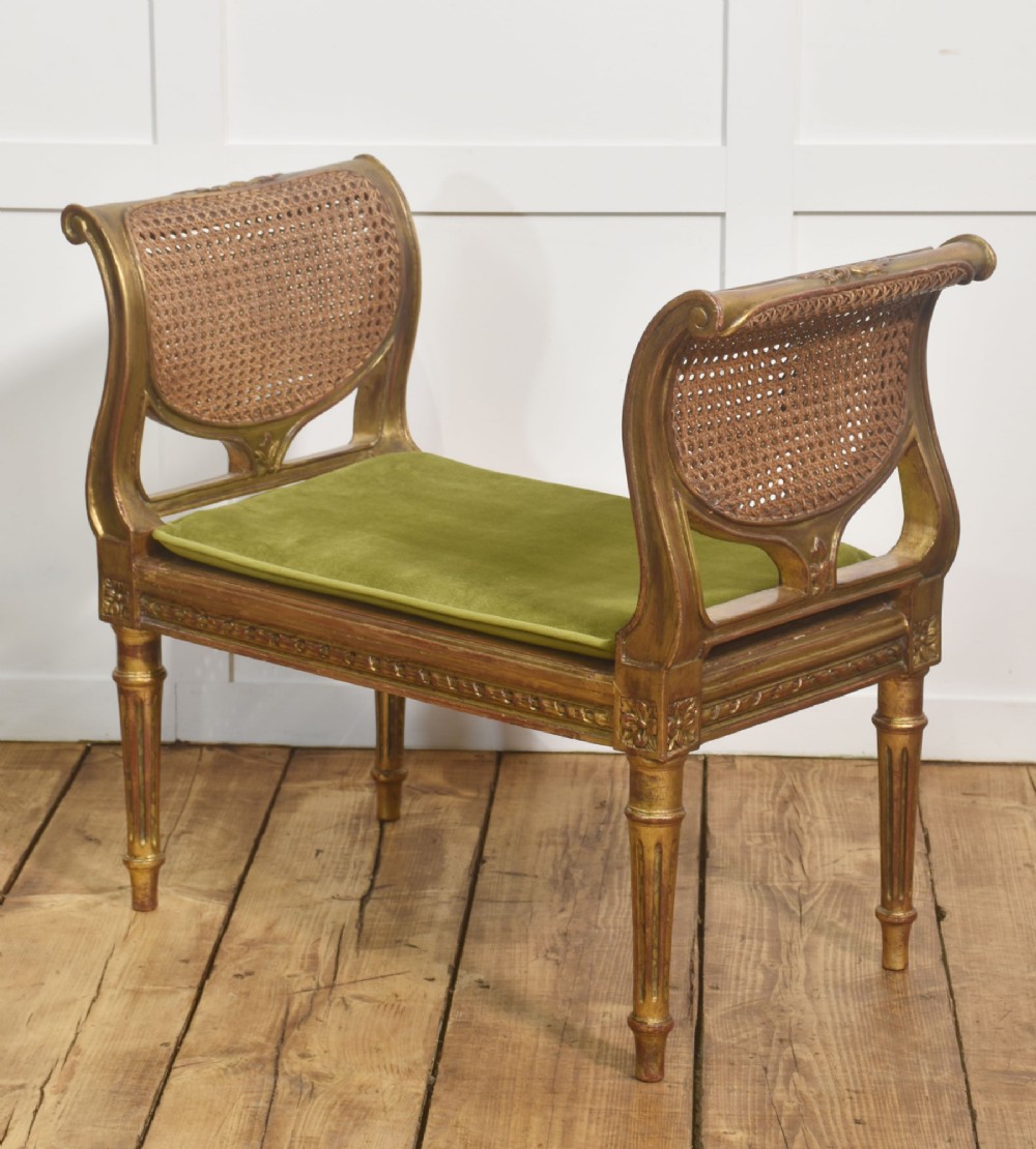 A Louis XVI style giltwood window stool featuring raised caned sides, fluted tapered legs, carved rosette accents, and a fitted olive green velvet cushion. View III