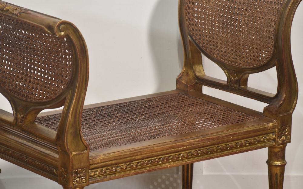 A Louis XVI style giltwood window stool featuring raised caned sides, fluted tapered legs, carved rosette accents, and a fitted olive green velvet cushion. View V