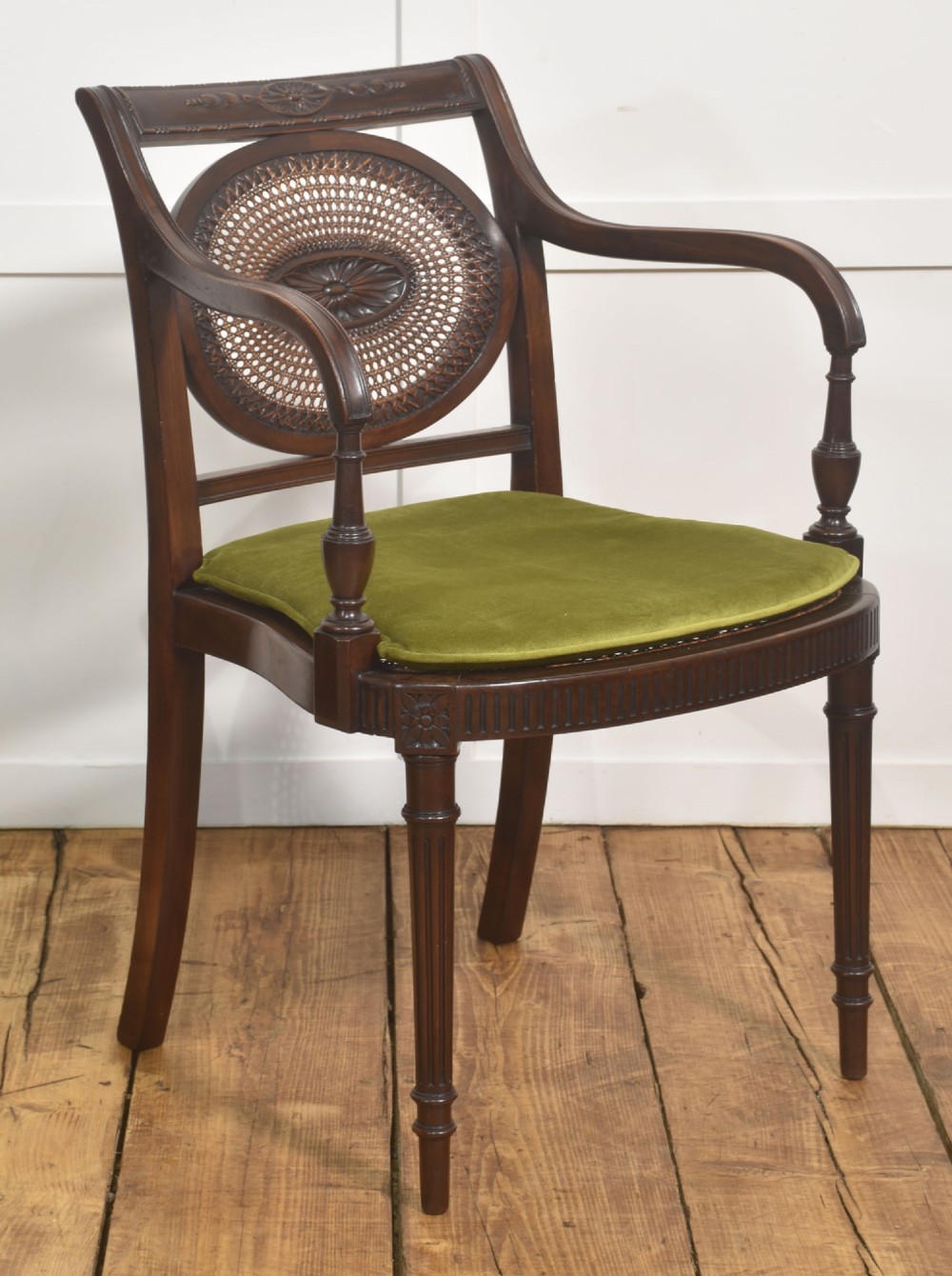 Sheraton Revival mahogany armchair featuring an oval cane back panel with carved central medallion, olive green velvet seat cushion, and turned fluted front legs.