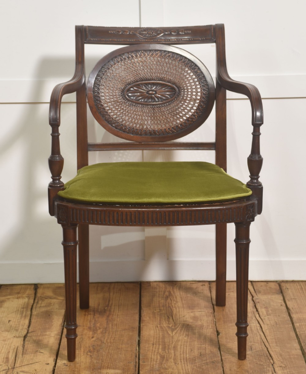Sheraton Revival mahogany armchair featuring an oval cane back panel with carved central medallion, olive green velvet seat cushion, and turned fluted front legs. View V