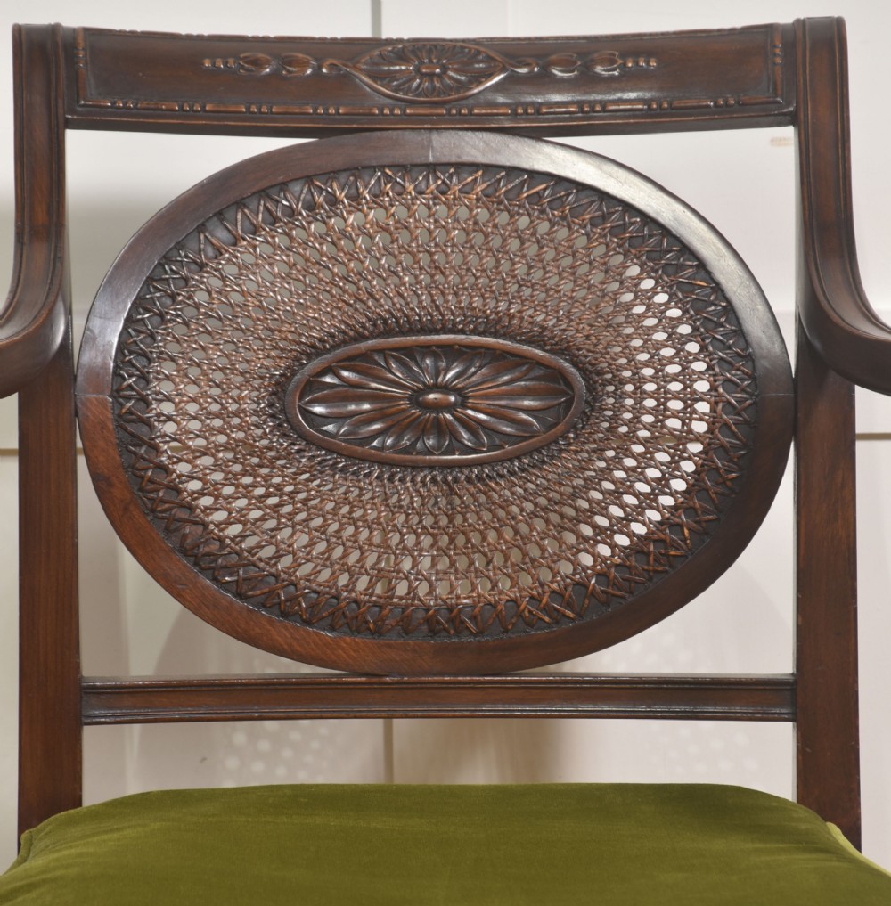 Sheraton Revival mahogany armchair featuring an oval cane back panel with carved central medallion, olive green velvet seat cushion, and turned fluted front legs. View VI