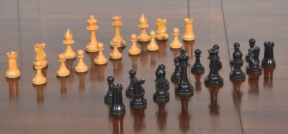 A late 19th-century Staunton chess set featuring natural light boxwood and ebonised black carved wooden pieces arrayed on a polished tabletop.