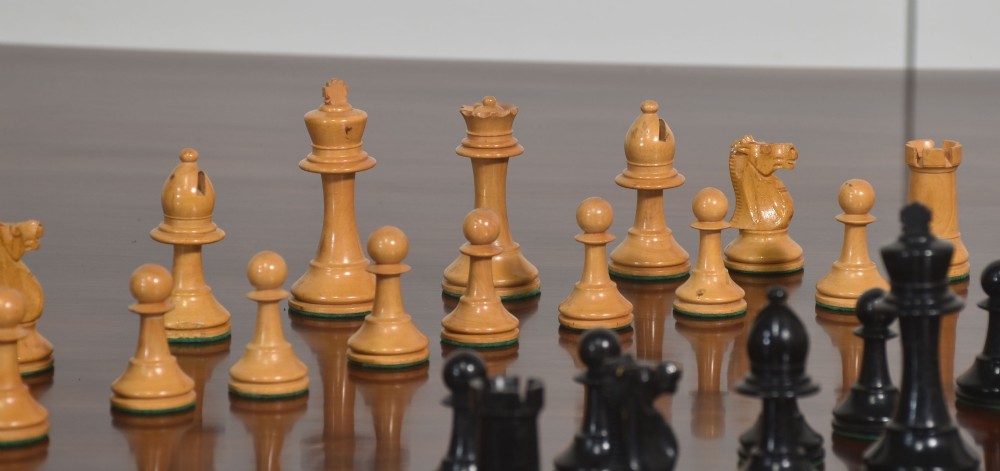 A late 19th-century Staunton chess set featuring natural light boxwood and ebonised black carved wooden pieces arrayed on a polished tabletop. View III