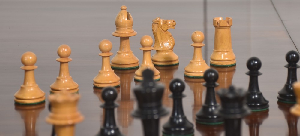 A late 19th-century Staunton chess set featuring natural light boxwood and ebonised black carved wooden pieces arrayed on a polished tabletop. View V