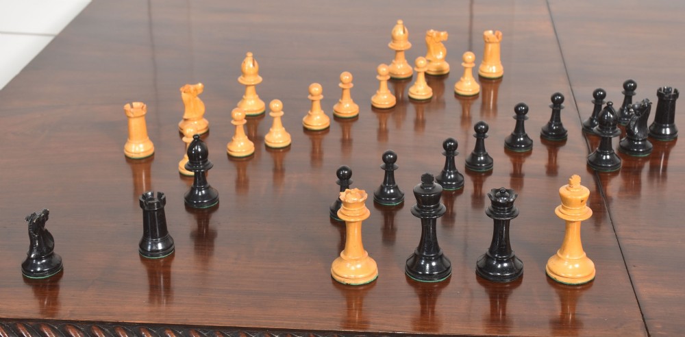 A late 19th-century Staunton chess set featuring natural light boxwood and ebonised black carved wooden pieces arrayed on a polished tabletop. View VI