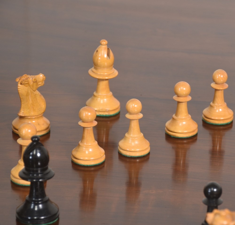 A late 19th-century Staunton chess set featuring natural light boxwood and ebonised black carved wooden pieces arrayed on a polished tabletop. View VII