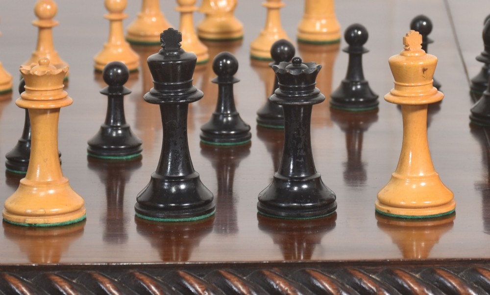 A late 19th-century Staunton chess set featuring natural light boxwood and ebonised black carved wooden pieces arrayed on a polished tabletop. View IX