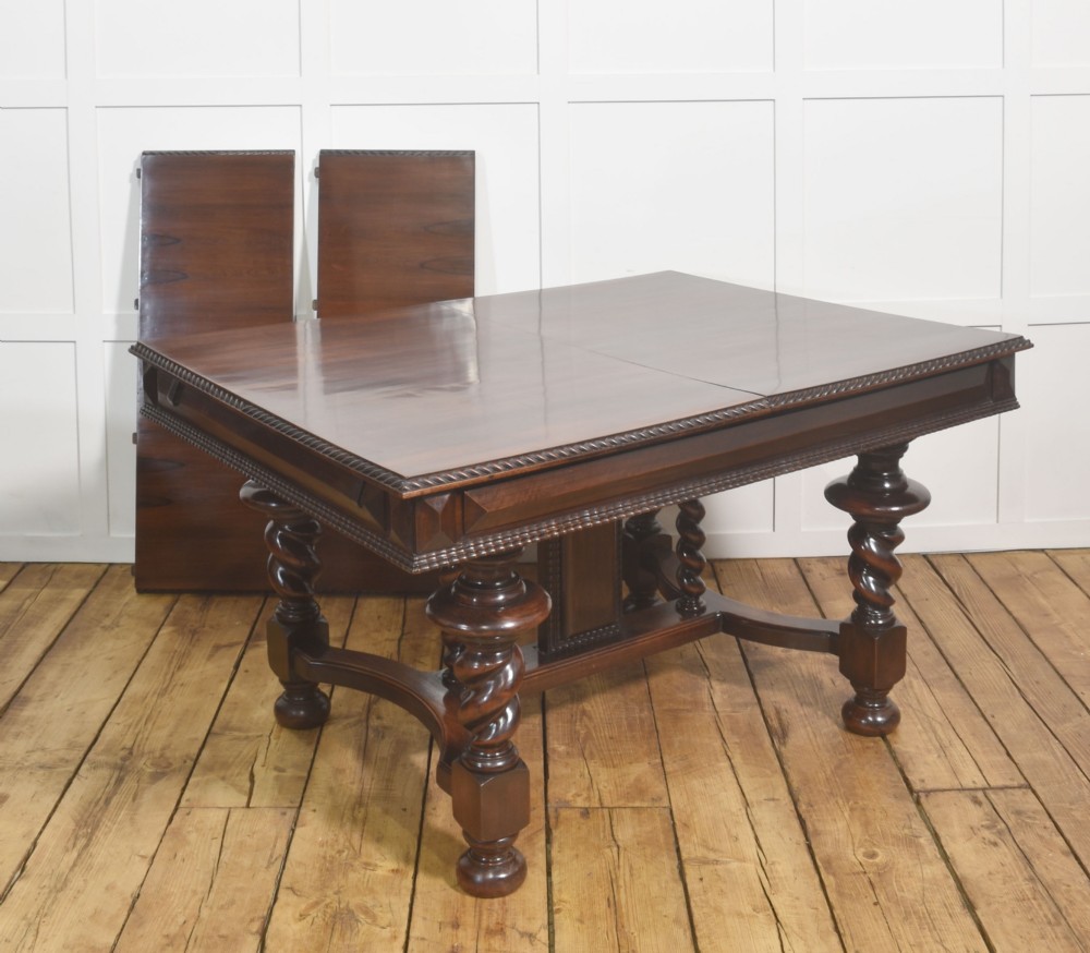 A large 19th-century Portuguese rosewood extending dining table with carved barley-twist legs, an H-stretcher base, and two removable extension leaves standing behind it.