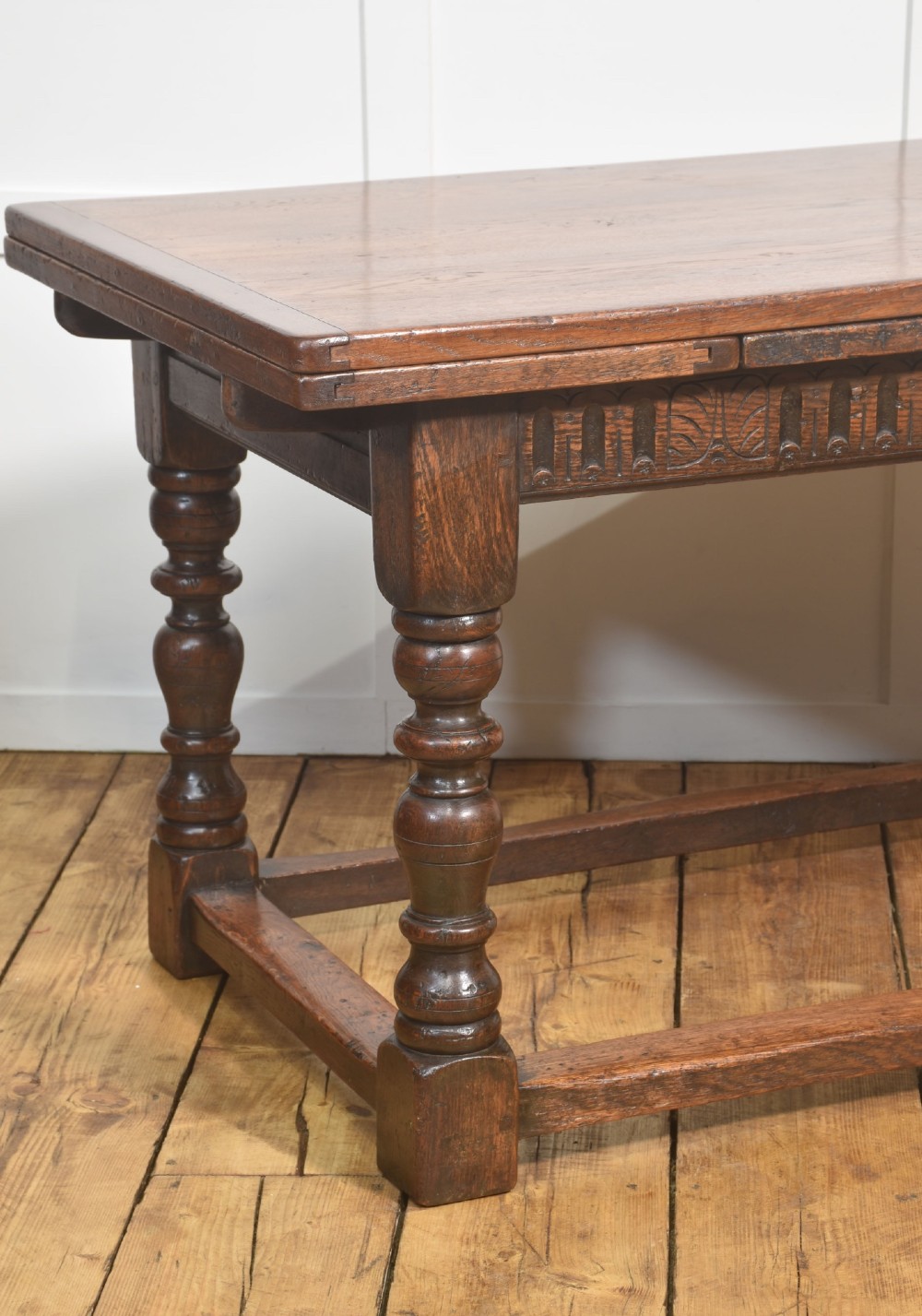 A dark oak Jacobean style draw-leaf dining table featuring carved frieze detailing along the apron, turned baluster legs, and a sturdy low box stretcher base. View IV