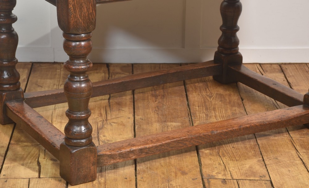 A dark oak Jacobean style draw-leaf dining table featuring carved frieze detailing along the apron, turned baluster legs, and a sturdy low box stretcher base. View V
