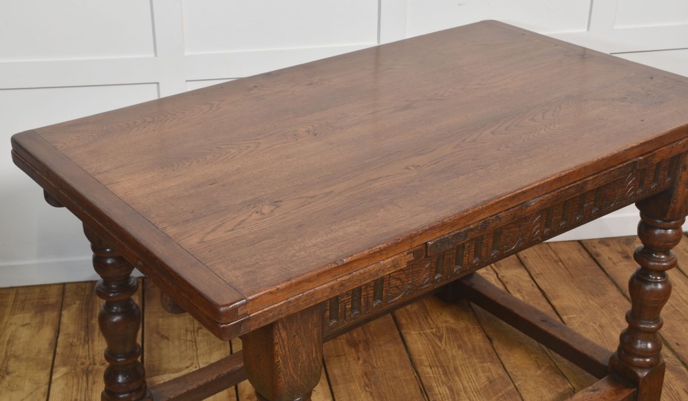 A dark oak Jacobean style draw-leaf dining table featuring carved frieze detailing along the apron, turned baluster legs, and a sturdy low box stretcher base. View VI