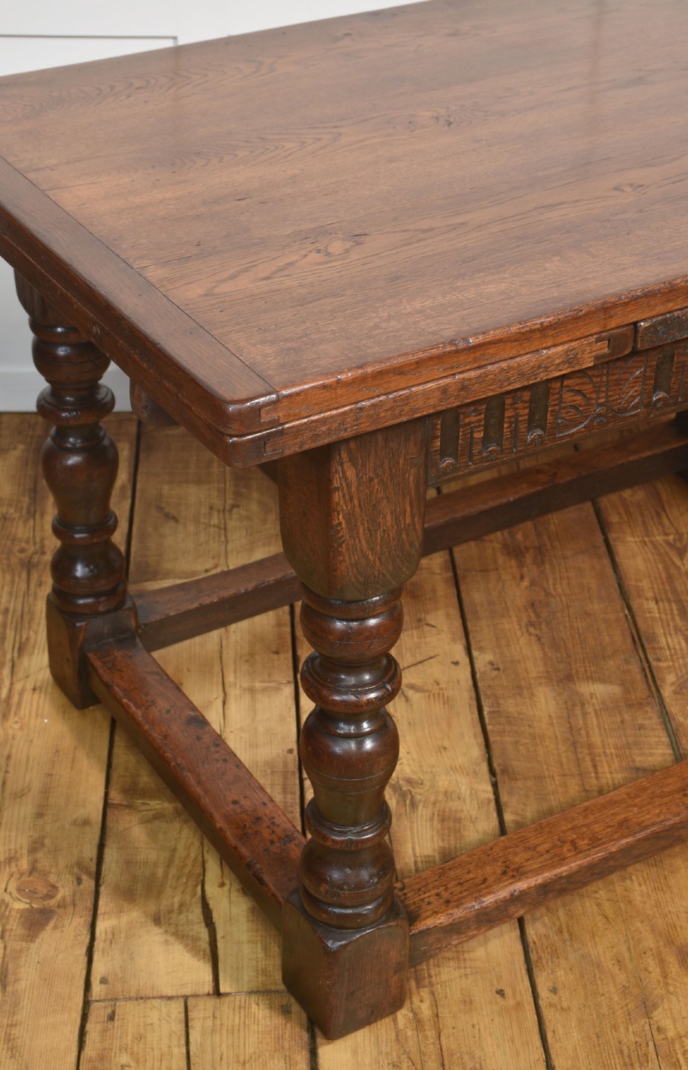 A dark oak Jacobean style draw-leaf dining table featuring carved frieze detailing along the apron, turned baluster legs, and a sturdy low box stretcher base. View VII