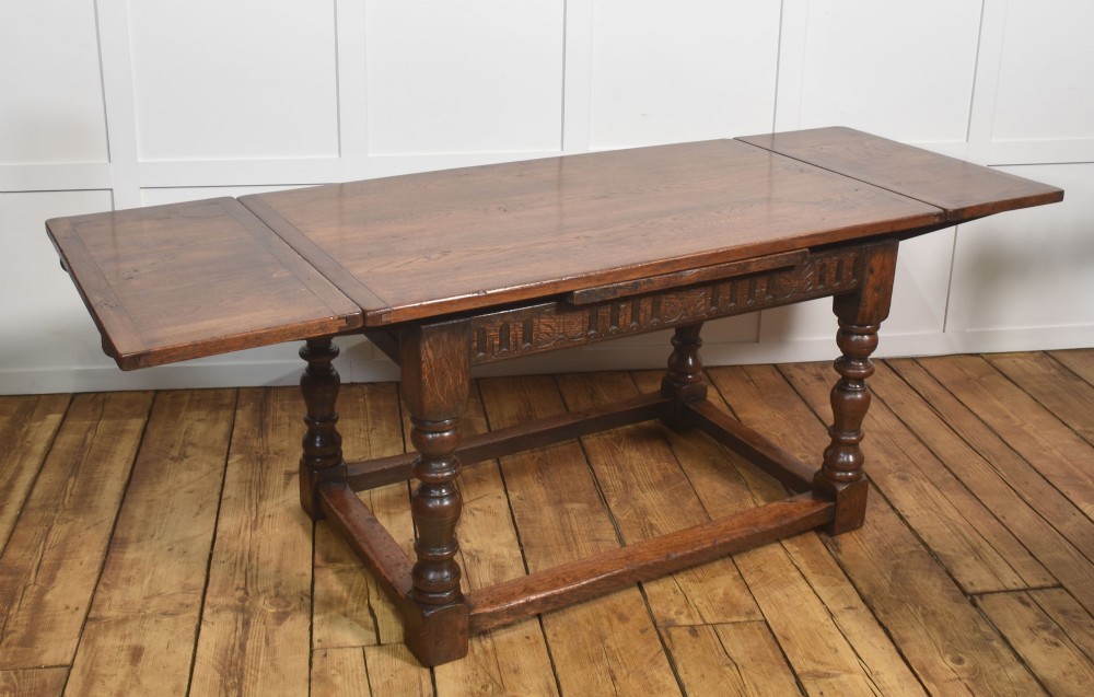 A dark oak Jacobean style draw-leaf dining table featuring carved frieze detailing along the apron, turned baluster legs, and a sturdy low box stretcher base. View VIII