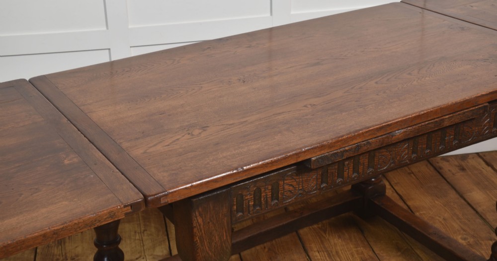 A dark oak Jacobean style draw-leaf dining table featuring carved frieze detailing along the apron, turned baluster legs, and a sturdy low box stretcher base. View IX