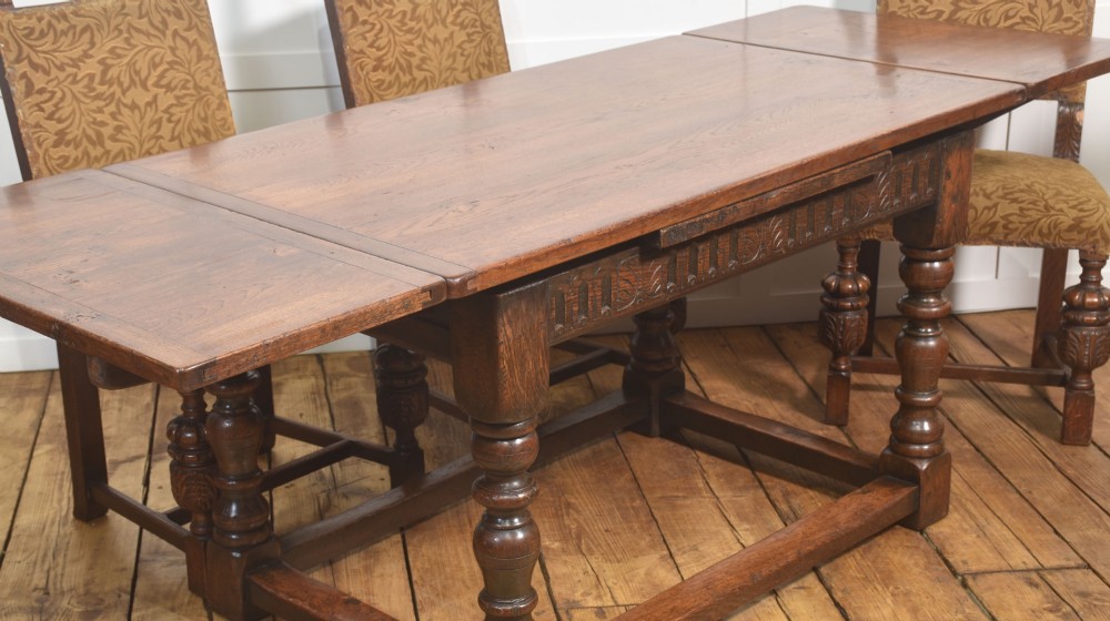 A dark oak Jacobean style draw-leaf dining table featuring carved frieze detailing along the apron, turned baluster legs, and a sturdy low box stretcher base. View XI