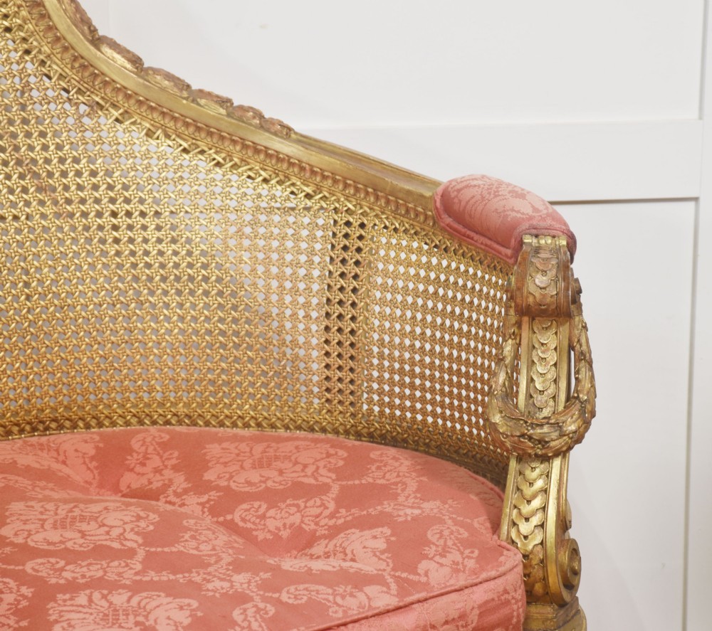 A French Louis XVI style giltwood settee featuring a woven cane backrest, carved fluted legs, and a rose-pink damask upholstered seat cushion. View VIII