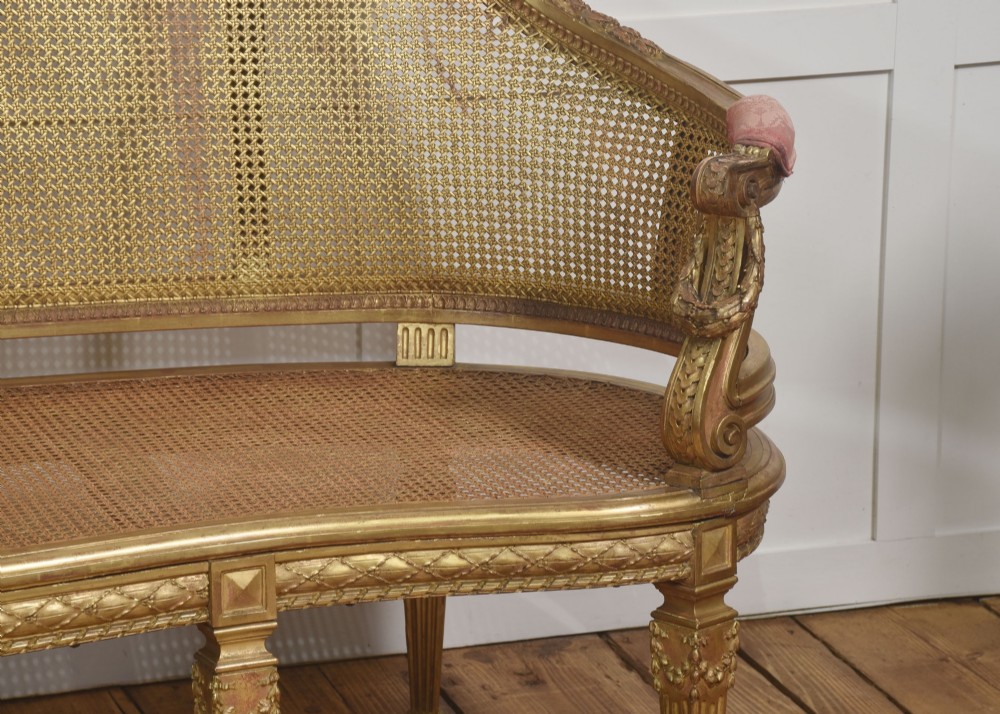 A French Louis XVI style giltwood settee featuring a woven cane backrest, carved fluted legs, and a rose-pink damask upholstered seat cushion. View XI