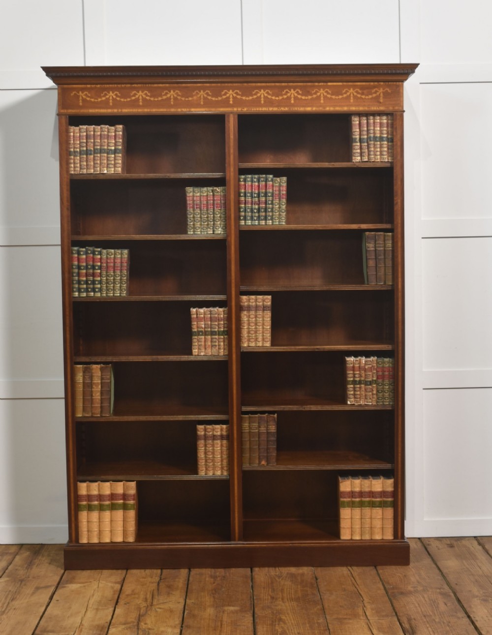 A tall, double-bay mahogany open bookcase featuring delicate satinwood festoon inlays along the top frieze and multiple fixed shelves containing books.