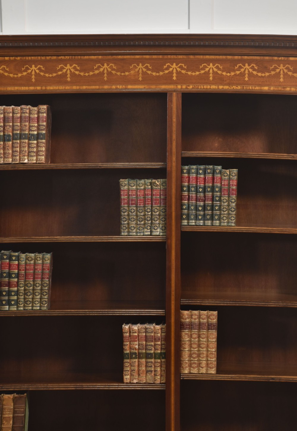 A tall, double-bay mahogany open bookcase featuring delicate satinwood festoon inlays along the top frieze and multiple fixed shelves containing books. View III