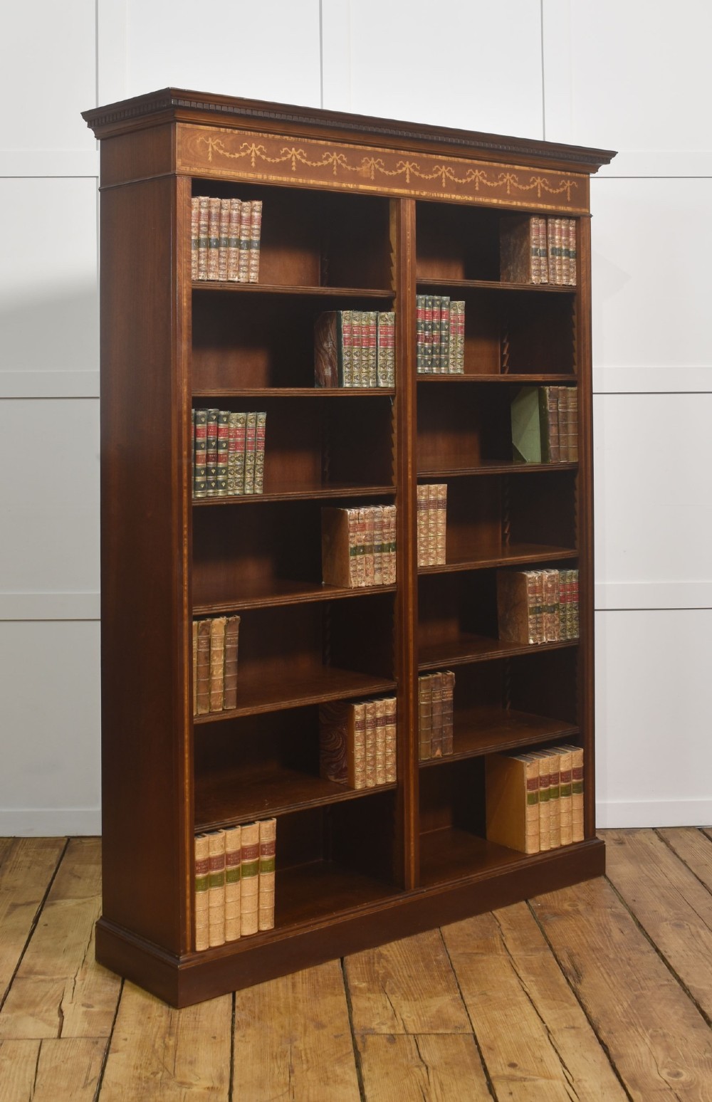 A tall, double-bay mahogany open bookcase featuring delicate satinwood festoon inlays along the top frieze and multiple fixed shelves containing books. View VI