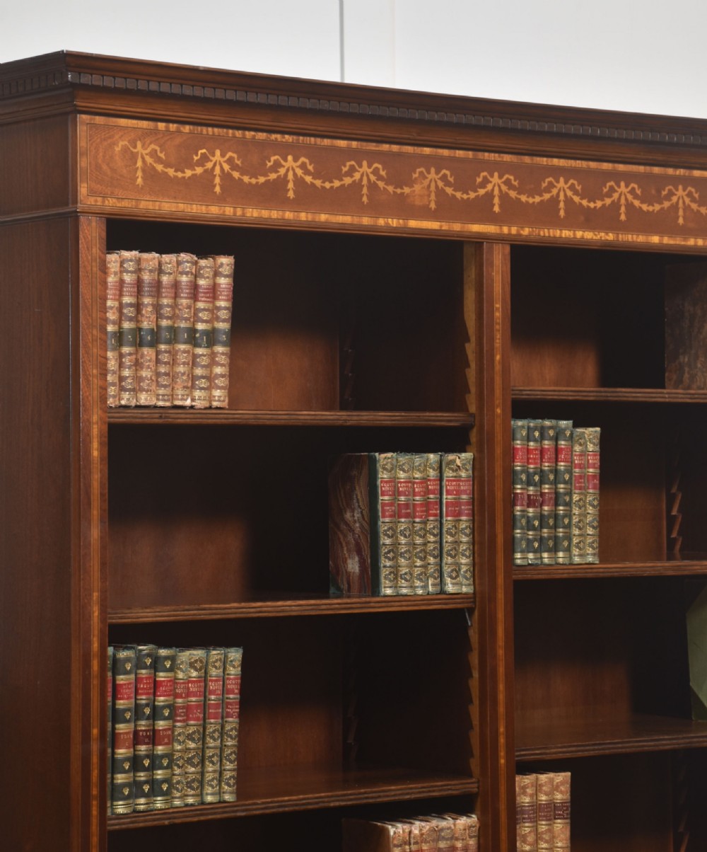 A tall, double-bay mahogany open bookcase featuring delicate satinwood festoon inlays along the top frieze and multiple fixed shelves containing books. View VII