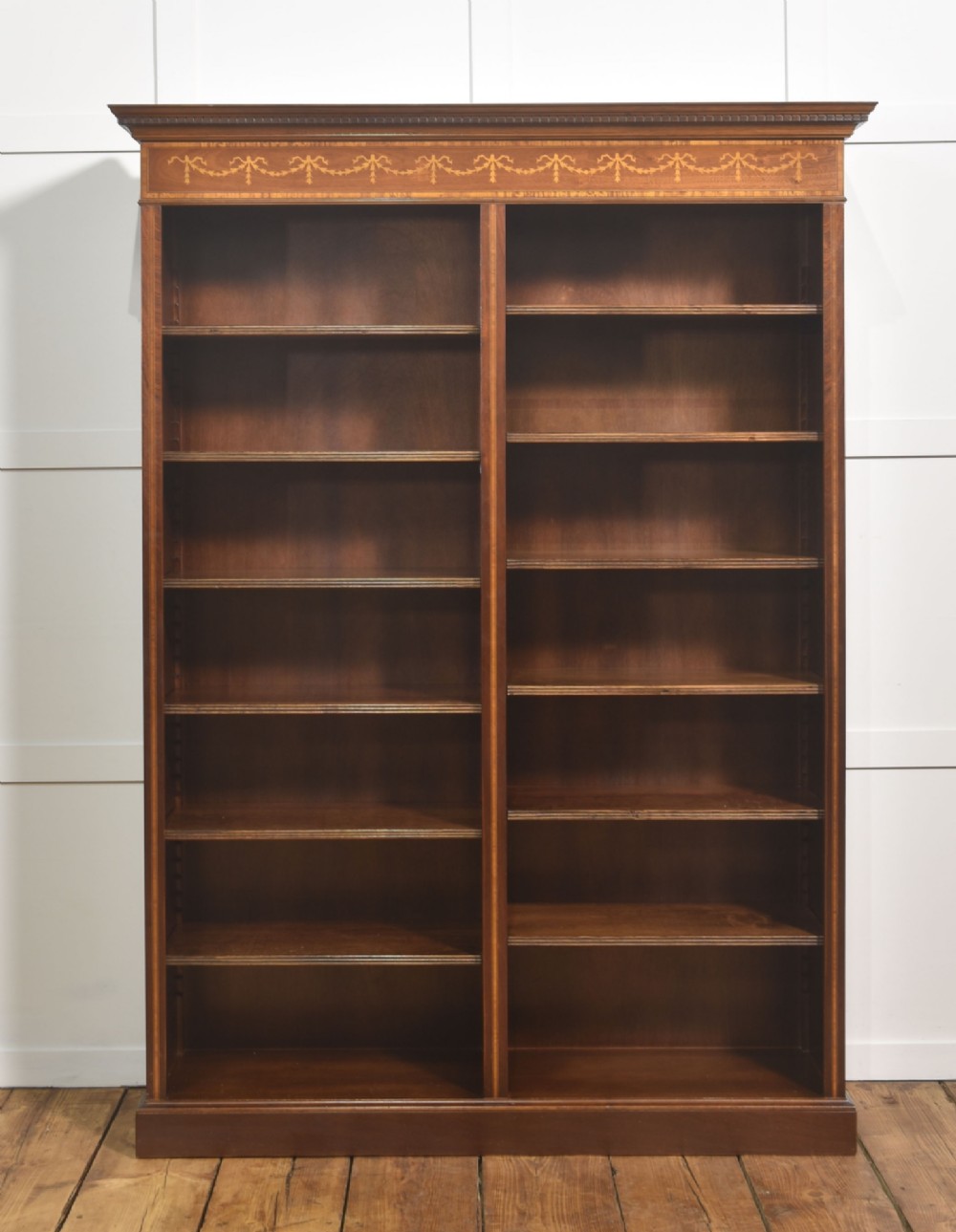 A tall, double-bay mahogany open bookcase featuring delicate satinwood festoon inlays along the top frieze and multiple fixed shelves containing books. View IX