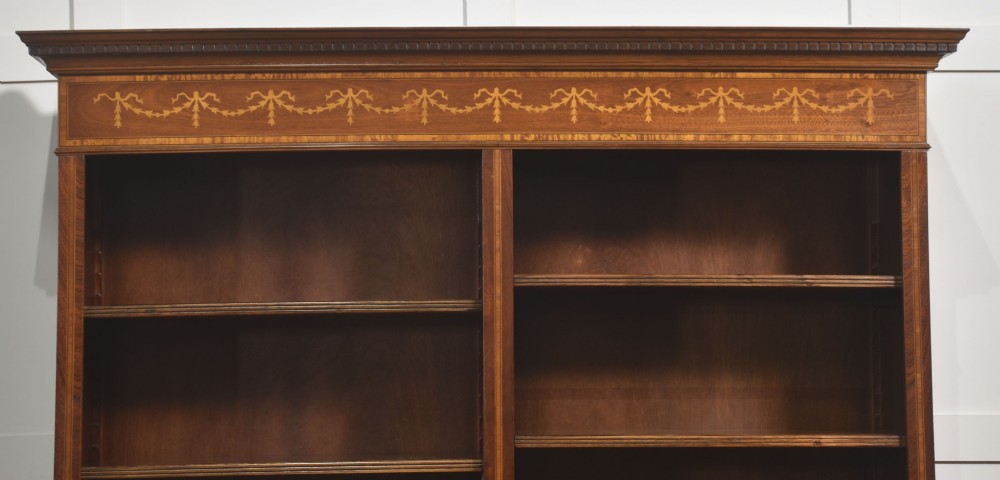 A tall, double-bay mahogany open bookcase featuring delicate satinwood festoon inlays along the top frieze and multiple fixed shelves containing books. View X