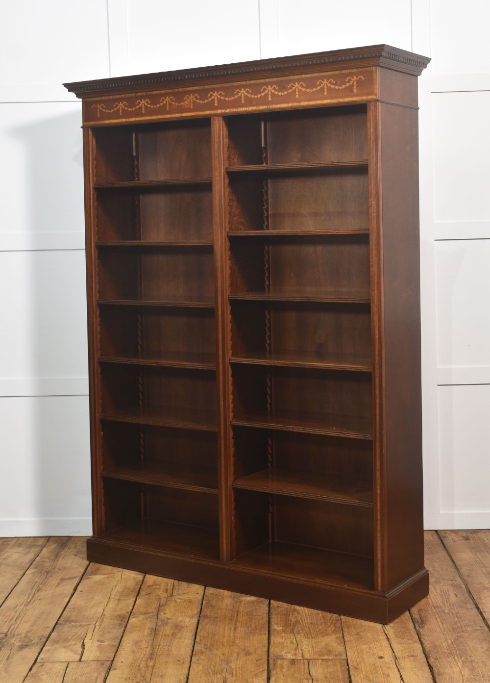 A tall, double-bay mahogany open bookcase featuring delicate satinwood festoon inlays along the top frieze and multiple fixed shelves containing books. View XI