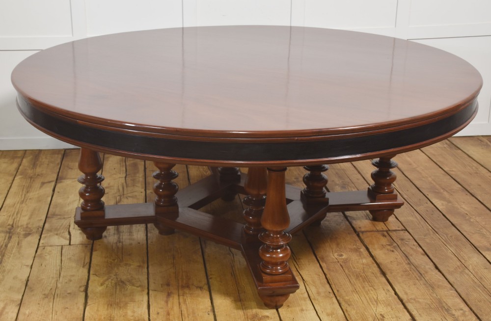 A large circular mahogany centre dining table with a polished surface, dark ebonised apron, and multiple turned legs supported by a cross-stretcher base.