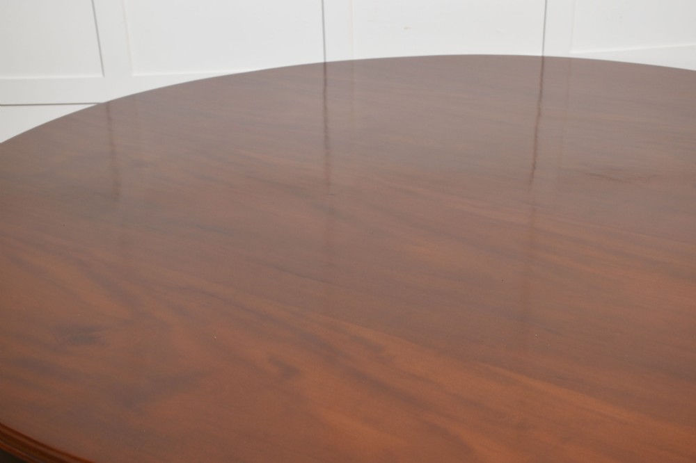 A large circular mahogany centre dining table with a polished surface, dark ebonised apron, and multiple turned legs supported by a cross-stretcher base. View IV