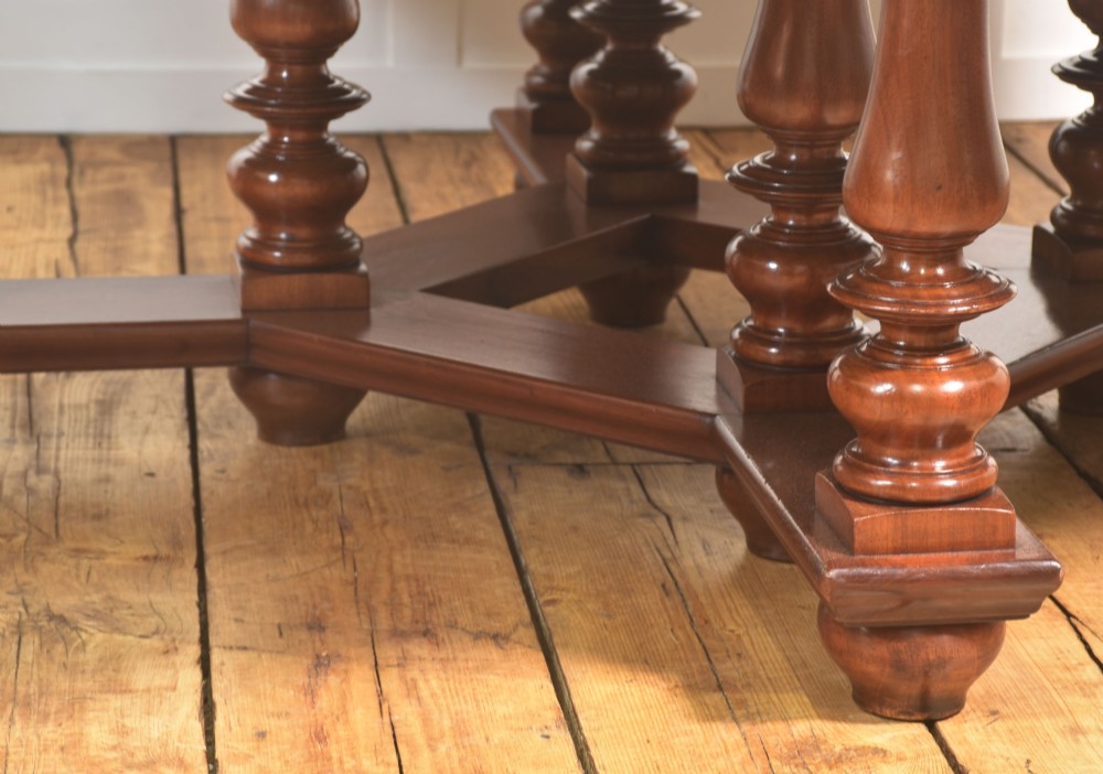 A large circular mahogany centre dining table with a polished surface, dark ebonised apron, and multiple turned legs supported by a cross-stretcher base. View VIII