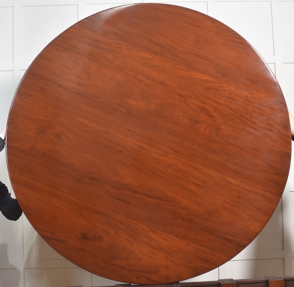 A large circular mahogany centre dining table with a polished surface, dark ebonised apron, and multiple turned legs supported by a cross-stretcher base. View IX