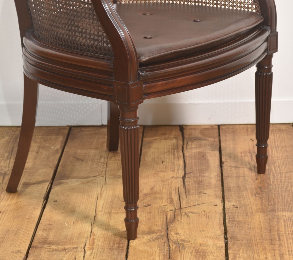 An Edwardian mahogany tub armchair featuring curved woven cane panels, a brown leather seat cushion, and fluted front legs. View III