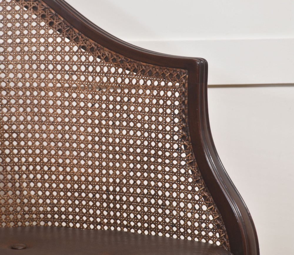 An Edwardian mahogany tub armchair featuring curved woven cane panels, a brown leather seat cushion, and fluted front legs. View IV