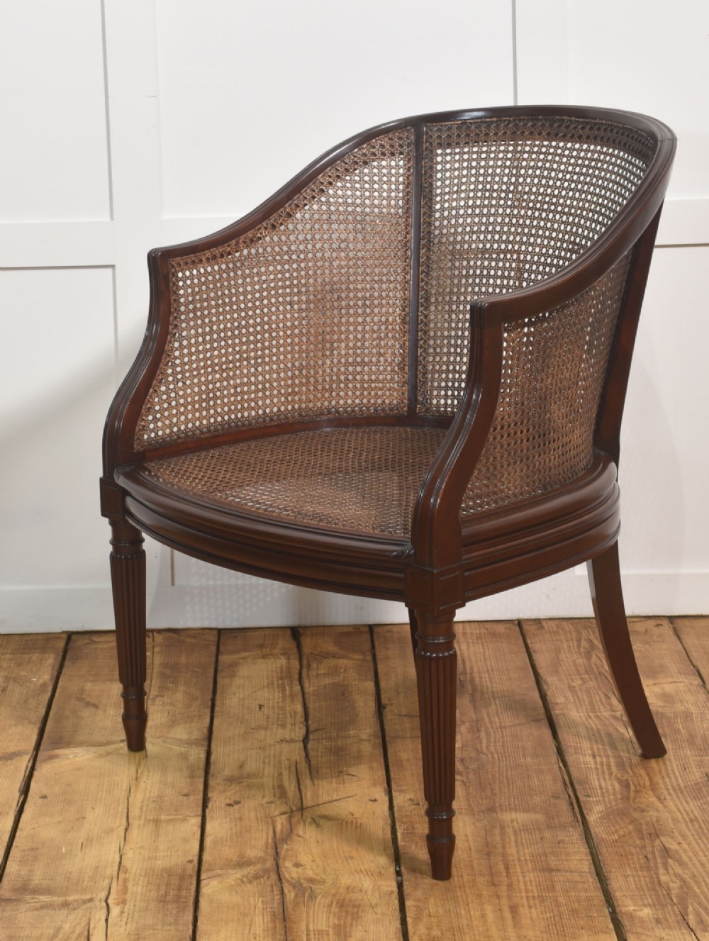 An Edwardian mahogany tub armchair featuring curved woven cane panels, a brown leather seat cushion, and fluted front legs. View VI