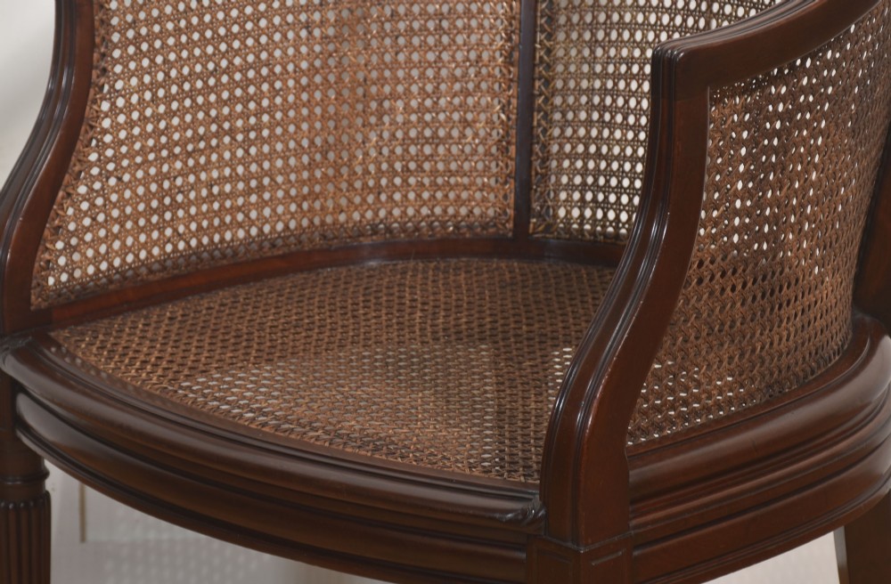 An Edwardian mahogany tub armchair featuring curved woven cane panels, a brown leather seat cushion, and fluted front legs. View VII