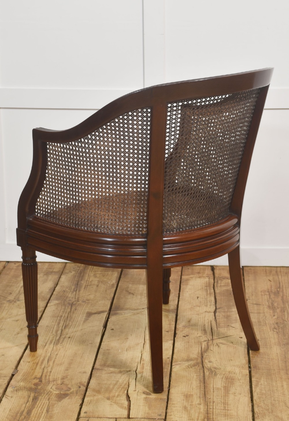 An Edwardian mahogany tub armchair featuring curved woven cane panels, a brown leather seat cushion, and fluted front legs. View VIII