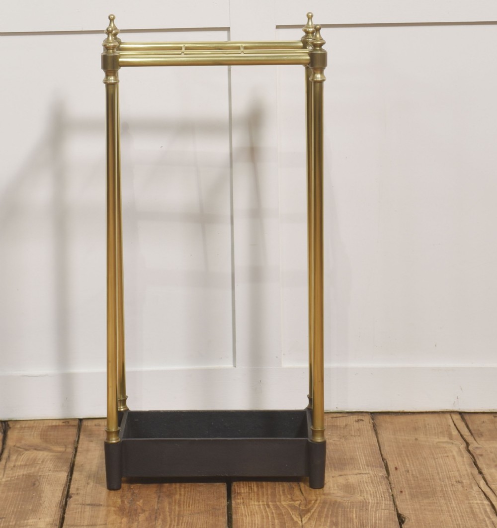 A 19th-century rectangular umbrella stand featuring brass upright posts, brass top rail dividers with corner finials, and a dark cast iron drip tray base. View V